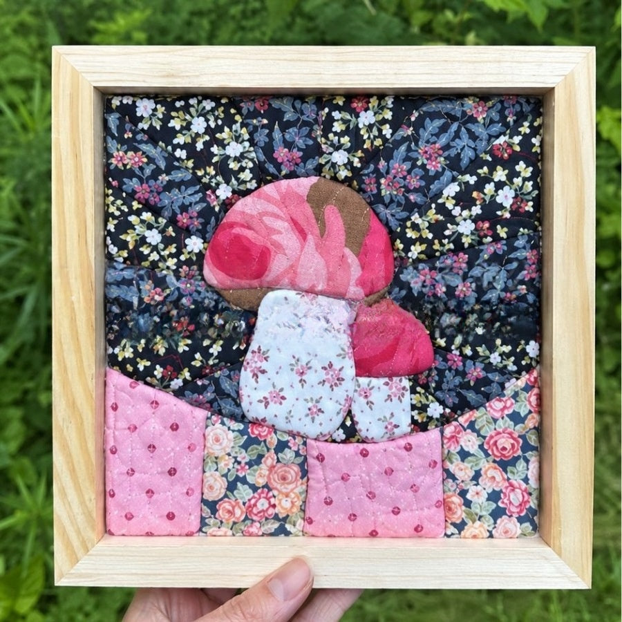 Red mushroom needlework shown in a square display frame as a finished project example.
