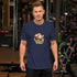 Lifestyle view of a person wearing the navy Bella+Canvas 3001 tee with the SLEIGH FUEL Santa coffee artwork centered on the front.